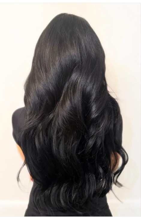 Long, glossy jet-black hair extensions styled in soft waves